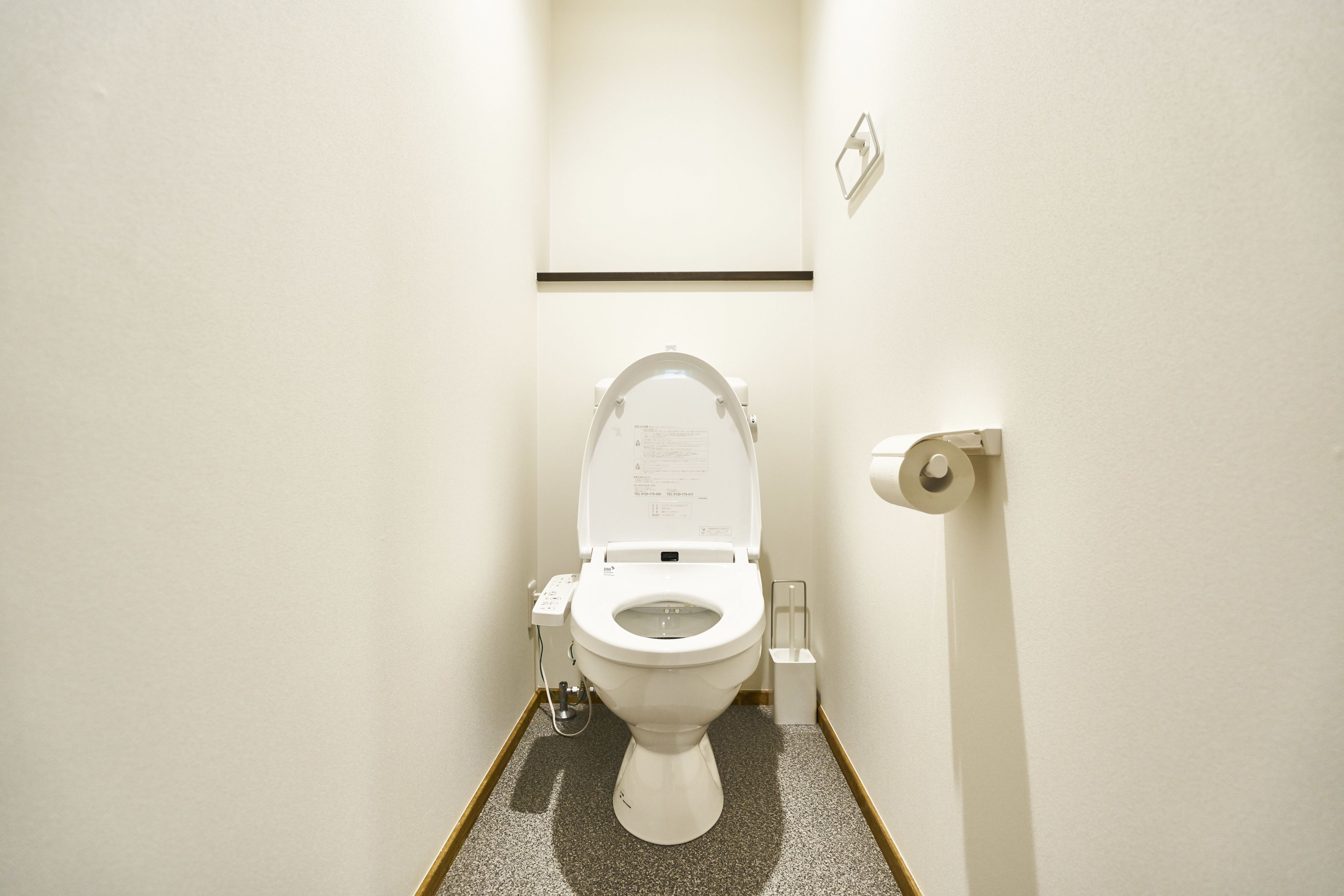 A small, clean bathroom with a white toilet, a wall-mounted flush handle, and a small trash bin.