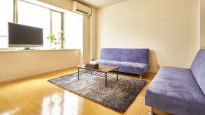 Un soggiorno moderno con una TV a schermo piatto, un divano viola, un tavolino da caffè e un'ampia finestra che fa entrare luce naturale.