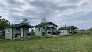 Three green wooden cabins with porches, each with a small deck and flower baskets. - Stuga på Nässjö Golfklubb (Nassjo)