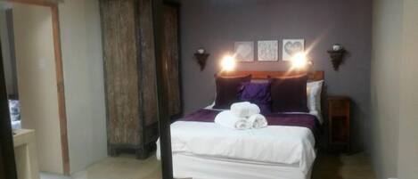 A bedroom with a bed, a wooden wardrobe, and wall-mounted lights.