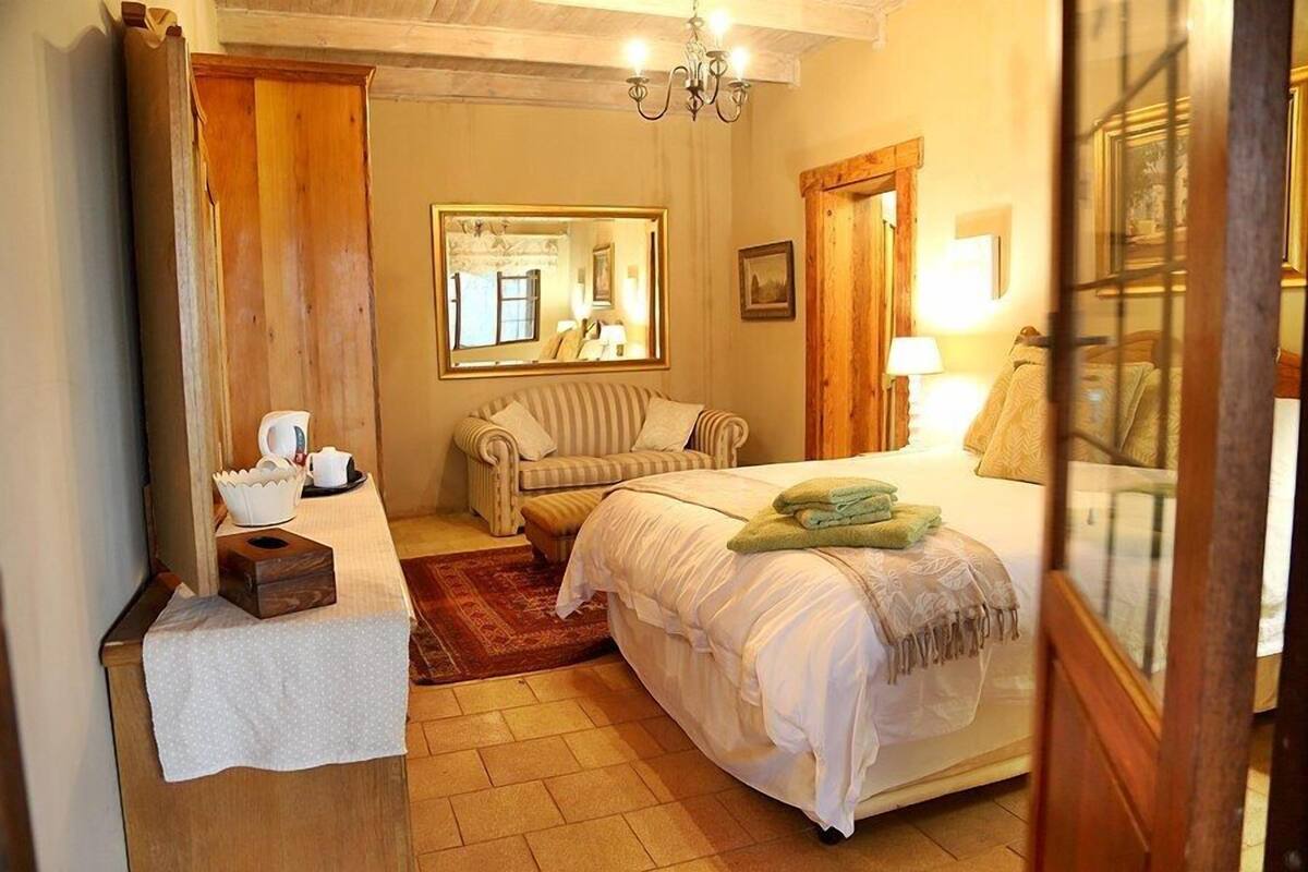 A cozy bedroom with a bed, a chair, a small table with a basket, a mirror, and a wooden door.