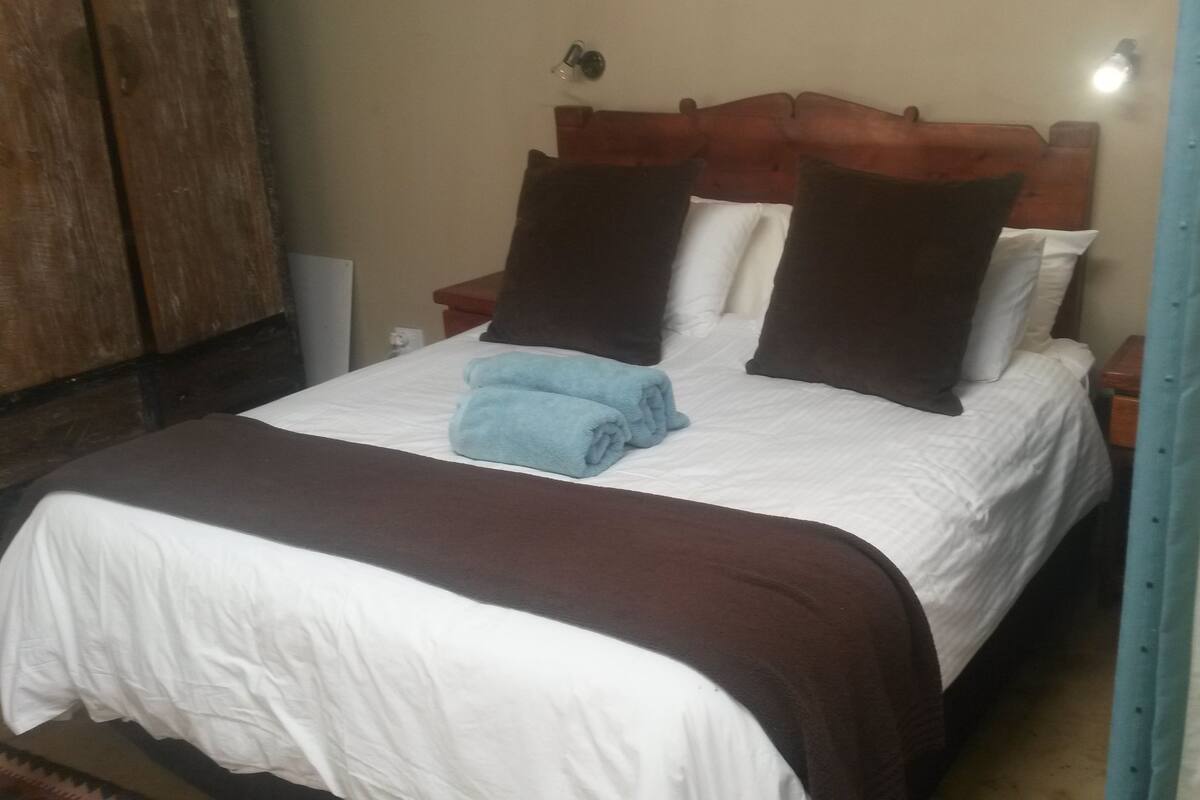 A bed with a brown headboard, white bedding, and two blue towels.