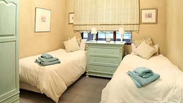 A bedroom with two single beds, a dresser, and a window with curtains.