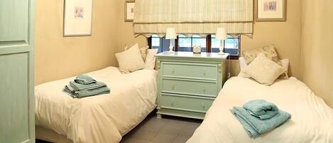 A bedroom with two single beds, a dresser, and a window with curtains.