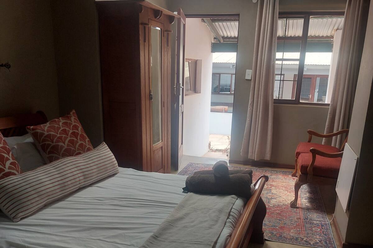A bedroom with a bed, a wardrobe, a chair, and a view of the outside.
