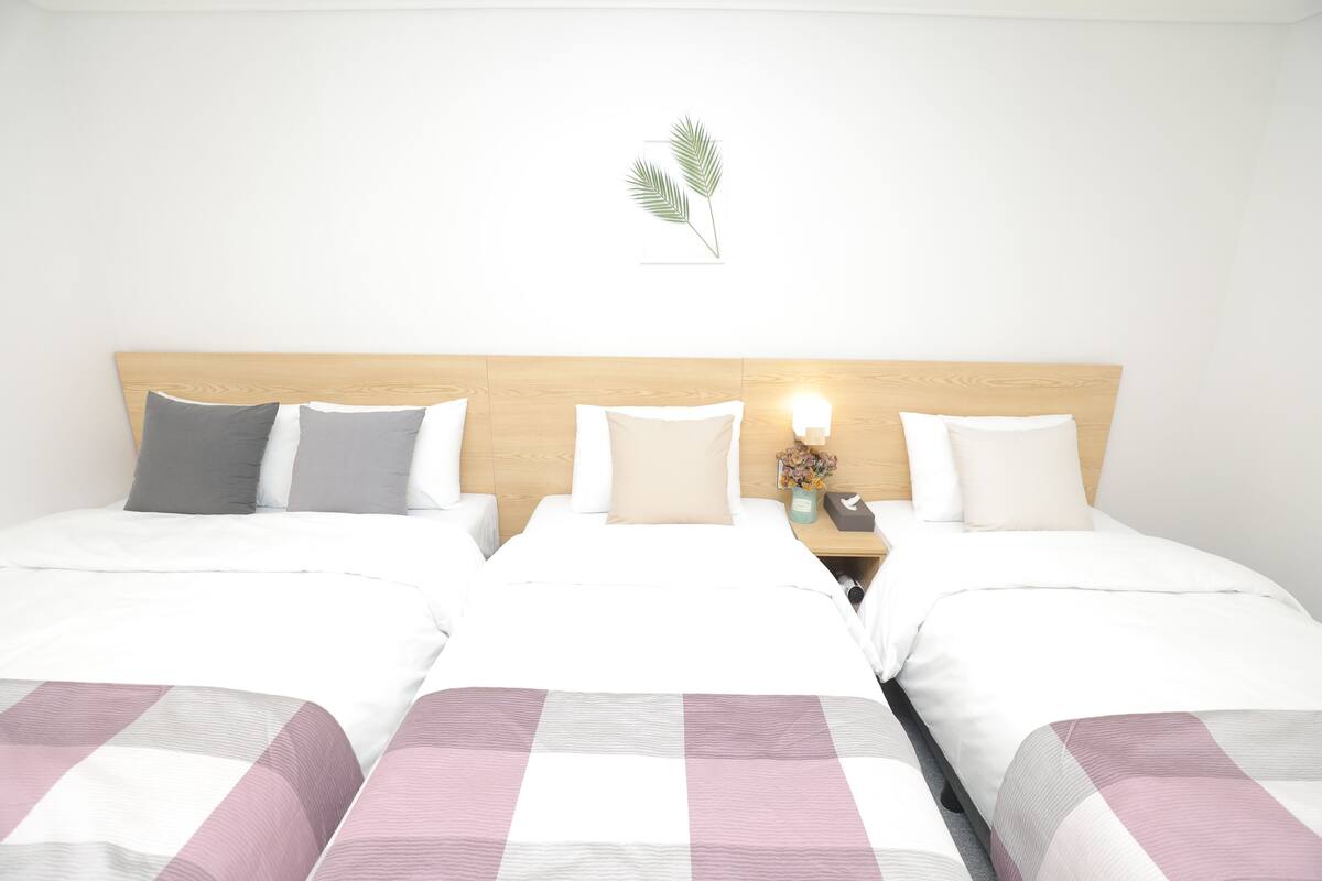 A hotel room with two beds, each with white bedding and a checkered blanket. There is a nightstand with a lamp and a vase of flowers.
