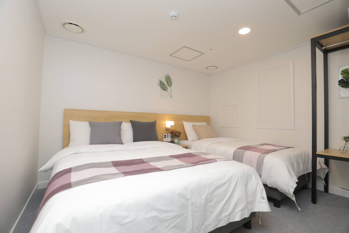 A hotel room with two beds, a wooden headboard, a nightstand with a lamp, and a mirror on the wall.