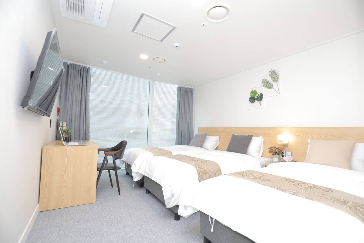 A hotel room with two beds, a desk with a laptop, a chair, a TV, and a window with curtains.