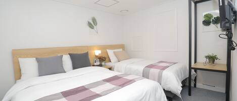 A hotel room with two beds, a wooden headboard, a desk with a chair, a TV mounted on the wall, and a small plant on the desk.