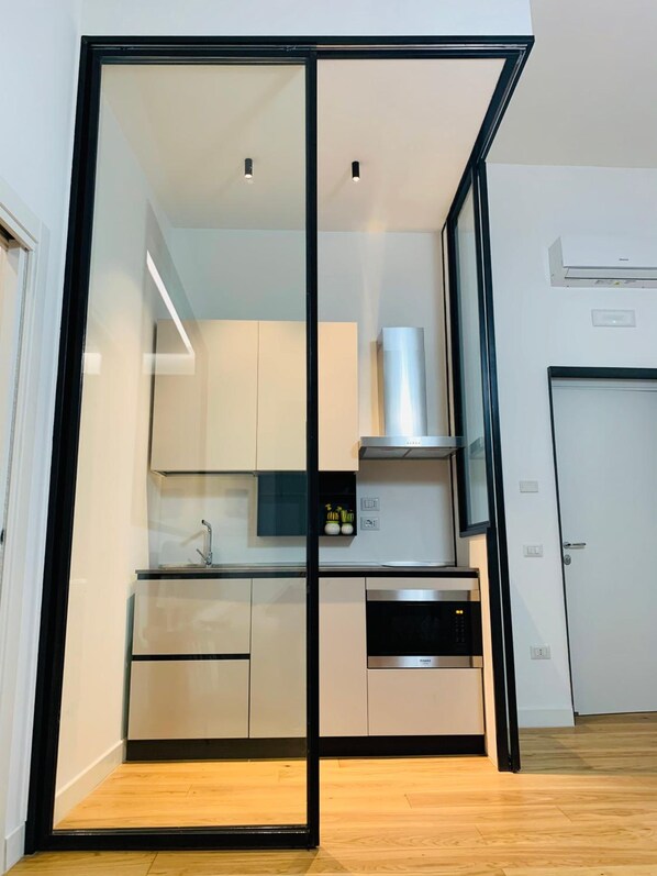 A modern kitchen with a glass partition, stainless steel appliances, and a wooden floor. - La Dimora Del Barone (Salerno)