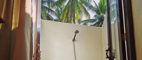 A shower area with a wooden wall, a hanging showerhead, and a shelf with a soap dispenser.