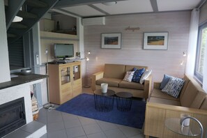 Ein modernes Wohnzimmer mit Sofa, Couchtisch und Kamin. Ein Fernseher steht auf einem Holzschrank, und an der Wand hängt ein Kunstwerk.