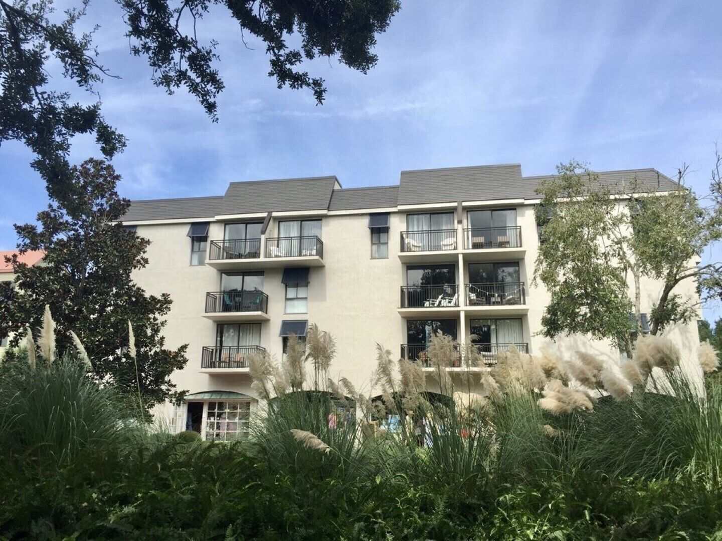 Un edificio residencial de varios pisos con balcones, rodeado de abundante vegetación.
