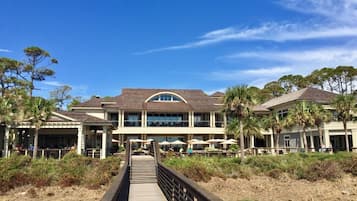 A beachfront hotel with a covered walkway leading to the entrance, surrounded by palm trees and a clear blue sky.