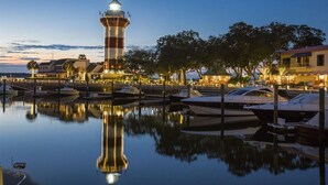 Un puerto deportivo frente al agua con un faro destacado, barcos amarrados y edificios a lo largo de la costa.