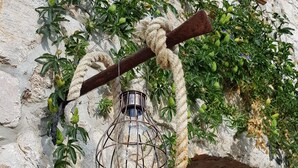 Un bâtiment rustique en pierre, doté d’une porte en bois et d’une lanterne suspendue à une branche par une corde.