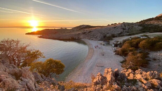 Un paysage côtier avec une plage, un terrain rocheux et un coucher de soleil.