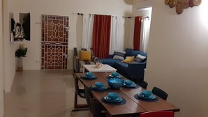 Un coin repas avec une table en bois dressée pour quatre personnes, des bols bleus et un canapé bleu avec des coussins en arrière-plan.