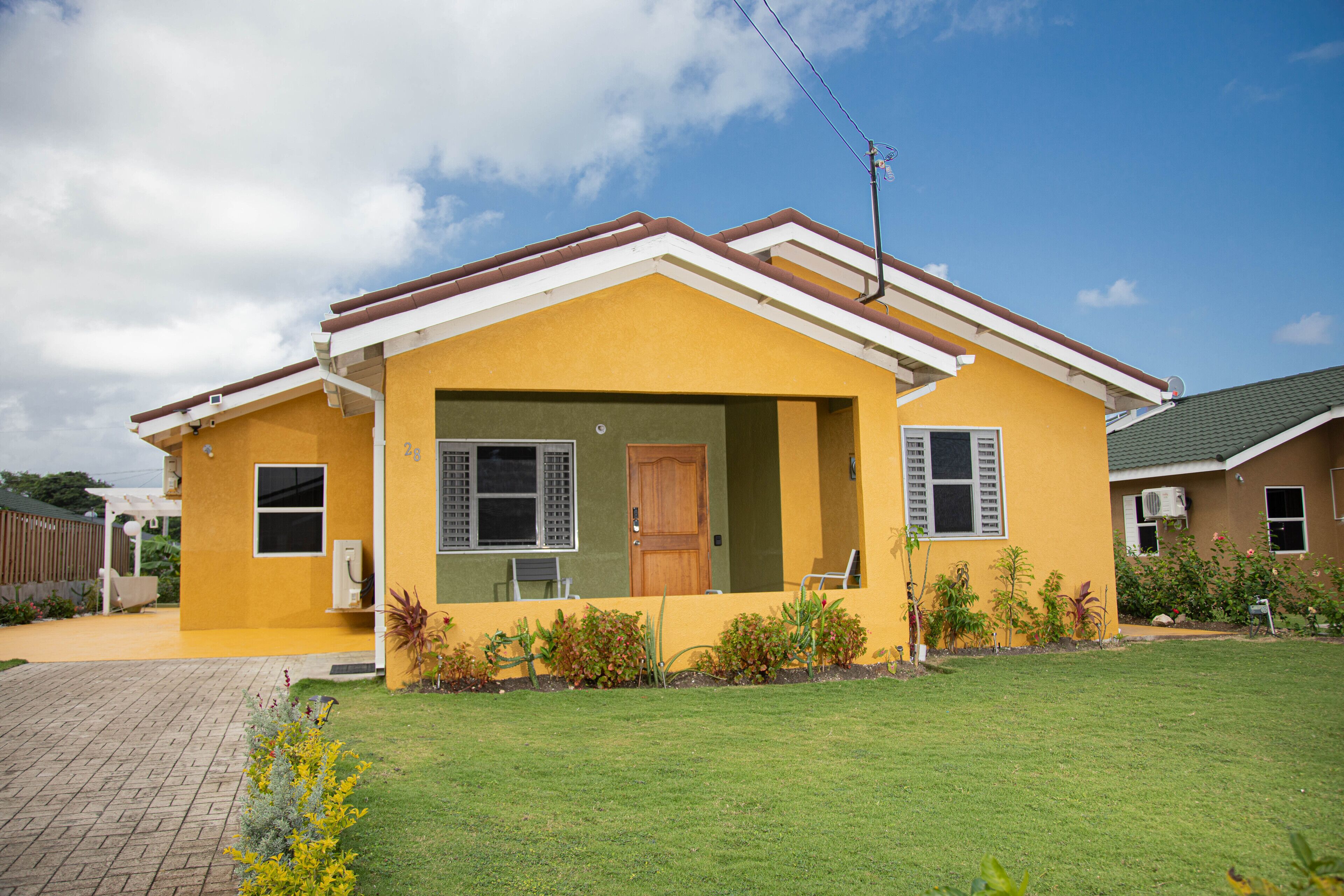 A yellow house with a brown roof, a front porch, and a small garden.
