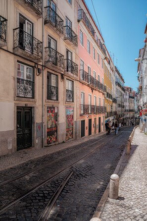 A cobblestone street with a tram track, buildings with balconies, and a clear blue sky. - Sitio dos Cavaleiros Apartments (Lisbon)