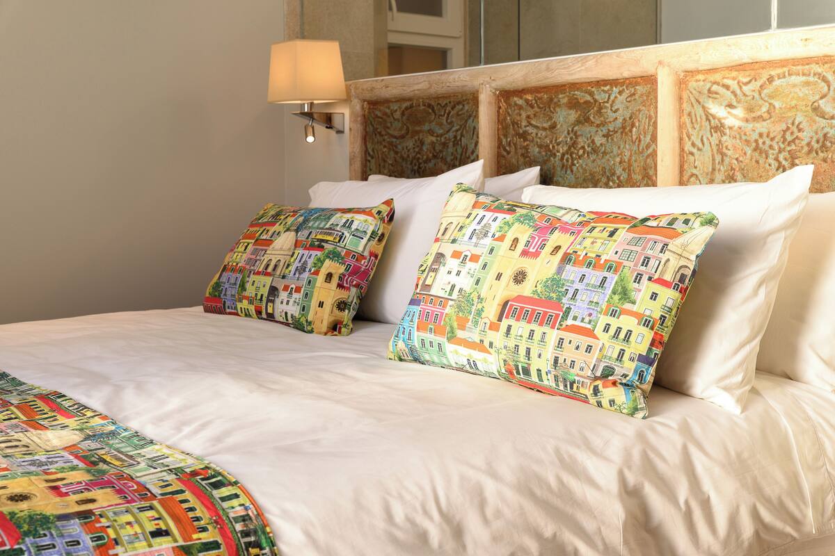 Una cama con sábanas blancas y almohadas estampadas de colores.