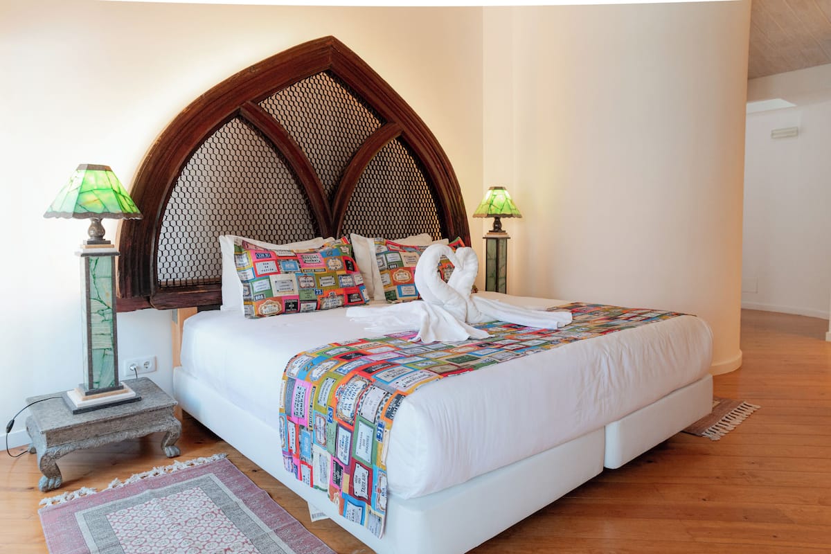 Una cama bien hecha con un cabecero decorativo, dos lámparas de noche y una colcha colorida.