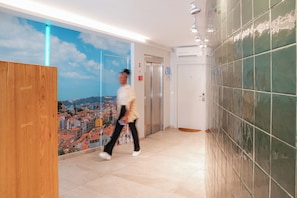 A hotel corridor with a cityscape mural, an elevator, and a tiled wall. - Sitio dos Cavaleiros Apartments (Lisbon)