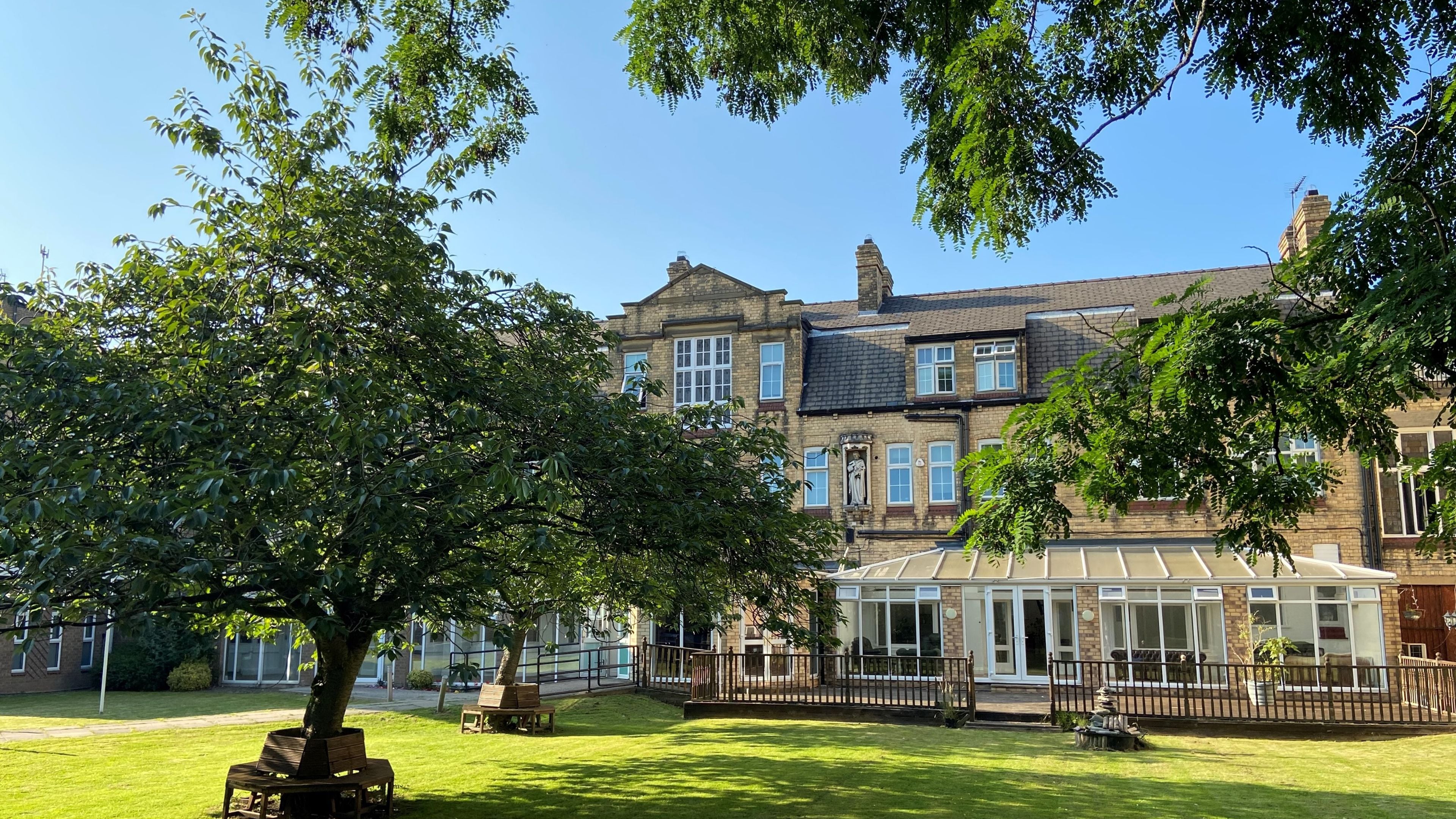 A traditional brick building with a conservatory, a lawn, and a large tree.