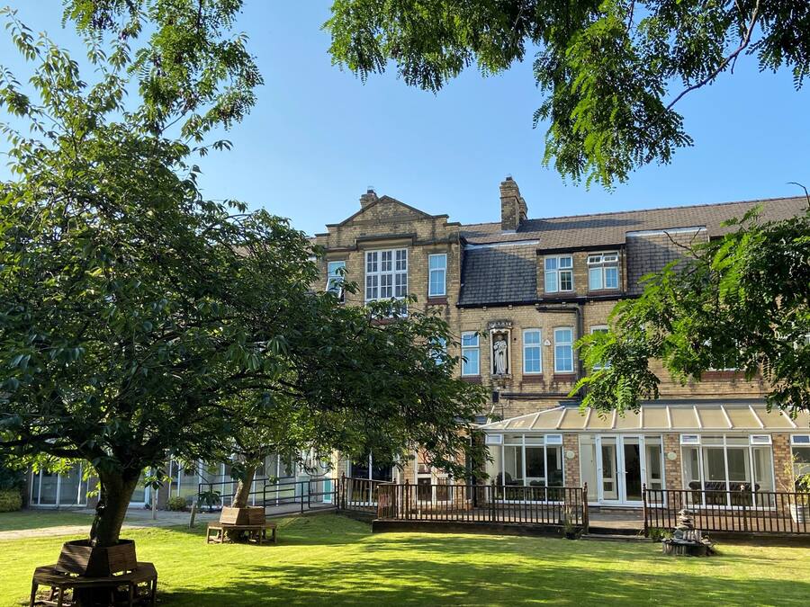 A traditional brick building with a conservatory, a lawn, and a large tree.