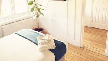 Un dormitorio con cama, televisor montado en la pared, planta en maceta y suelo de madera.