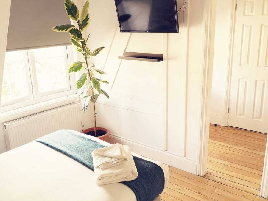 Un dormitorio con cama, televisor montado en la pared, planta en maceta y suelo de madera.