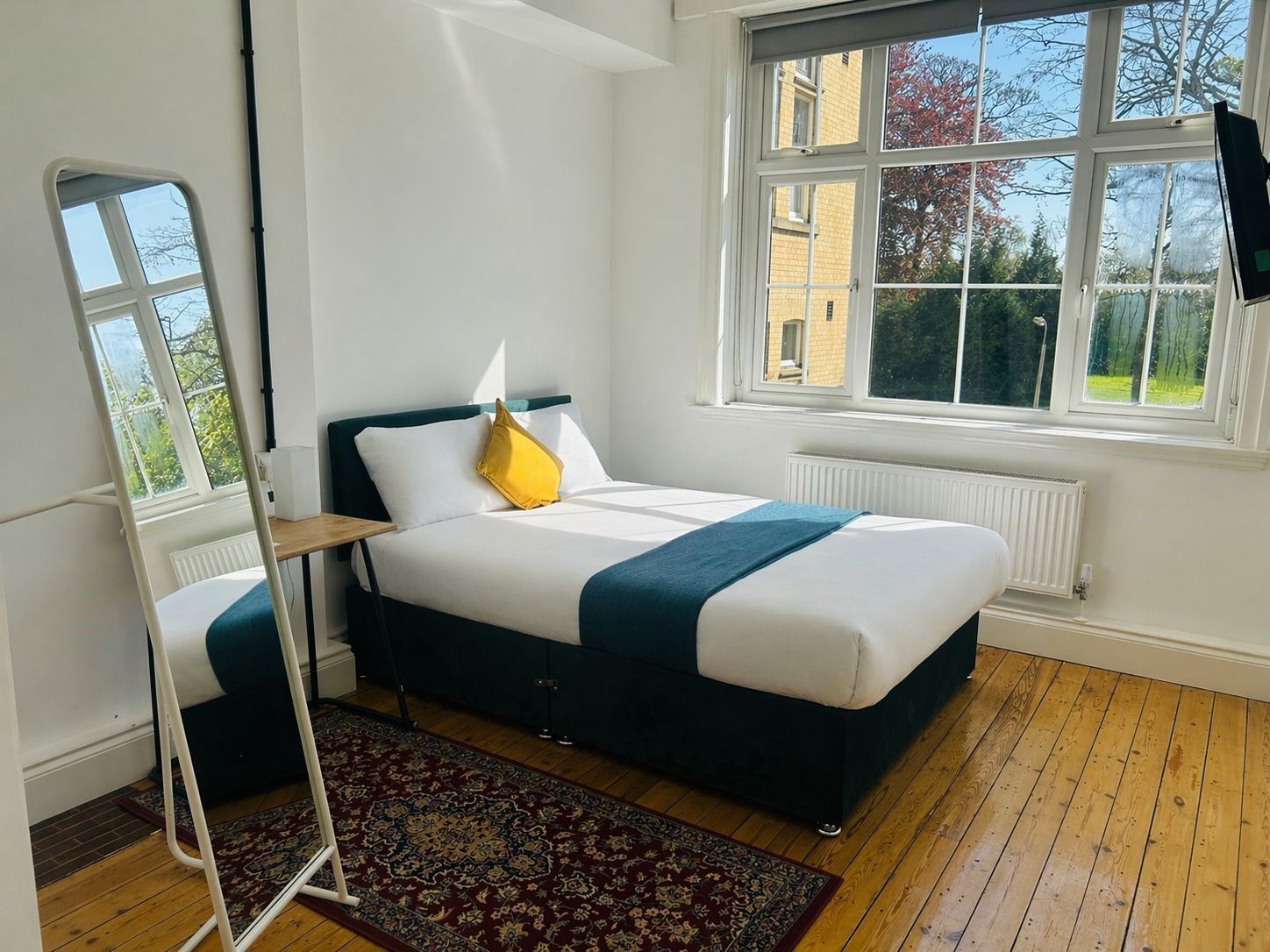 A bedroom with a bed, a window, a radiator, and a standing lamp.