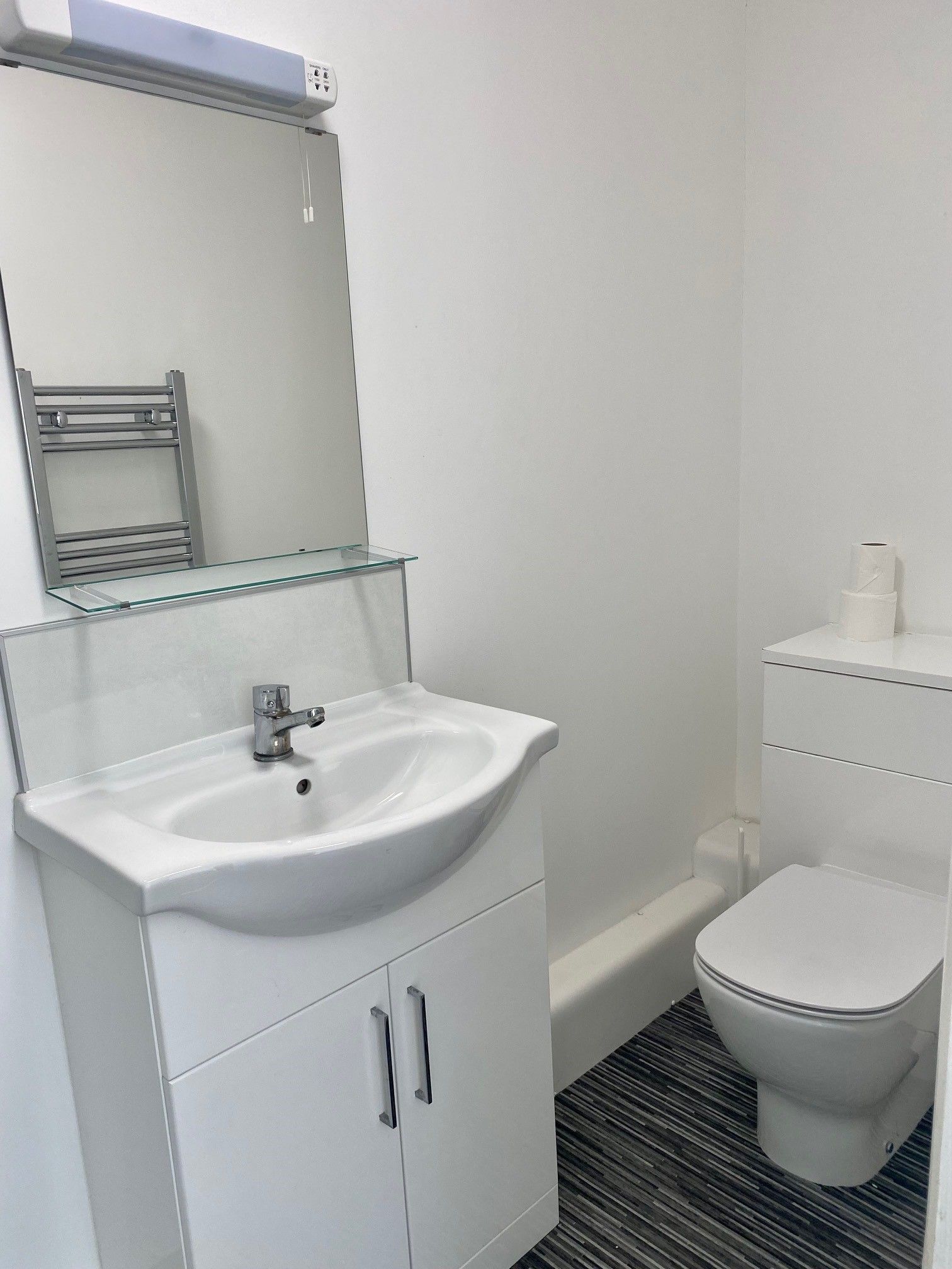 Un baño con lavamanos, espejo y retrete blancos.