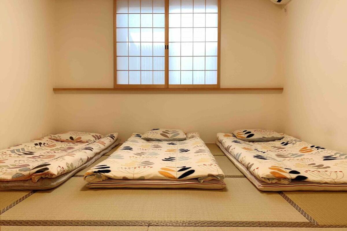 A room with three tatami mat beds, a sliding shoji screen window, and a ceiling-mounted air conditioner.