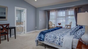 Un dormitorio con cama, escritorio, silla y baño visible a través de una puerta abierta.