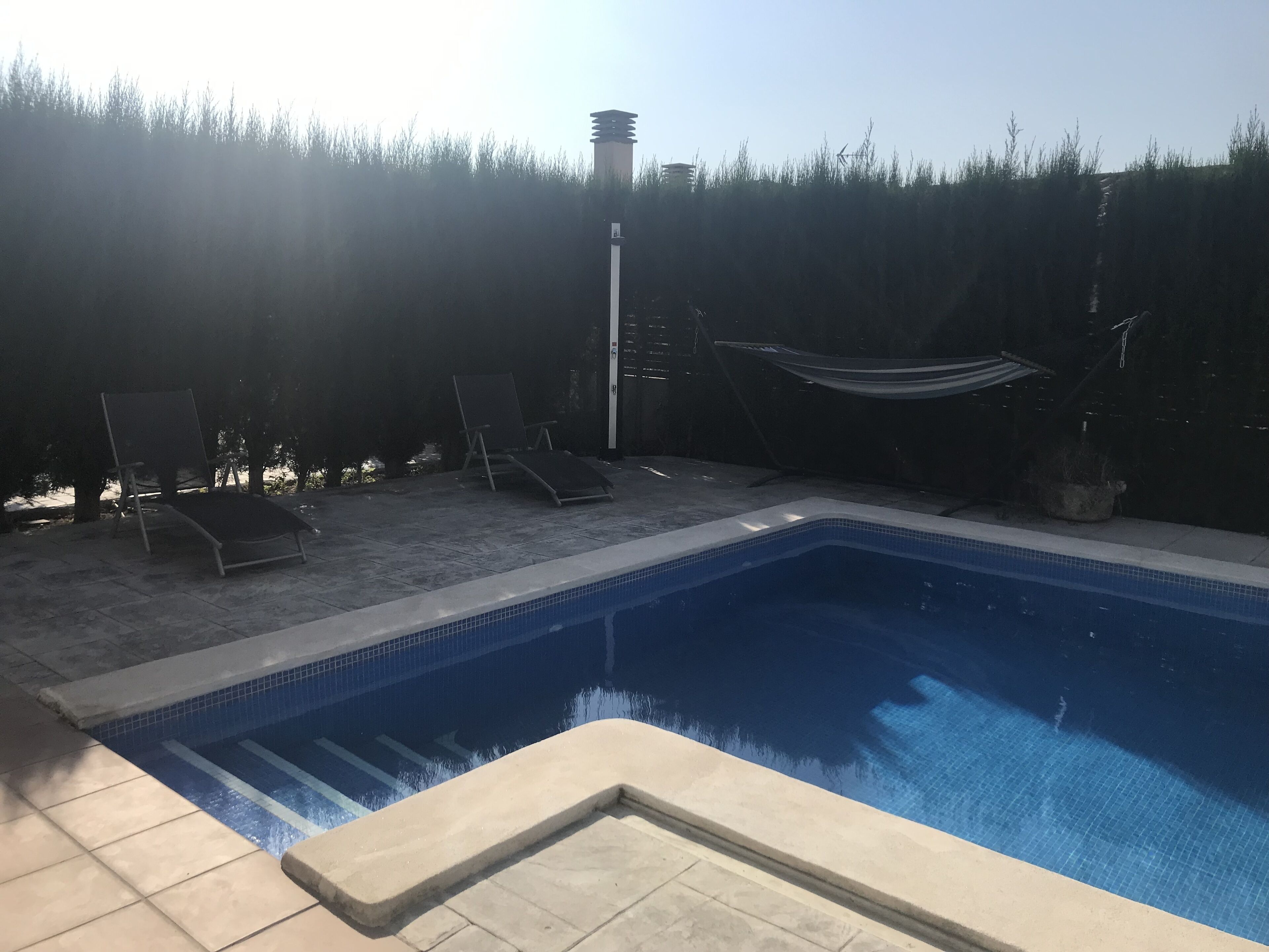 A swimming pool with lounge chairs and a hammock.