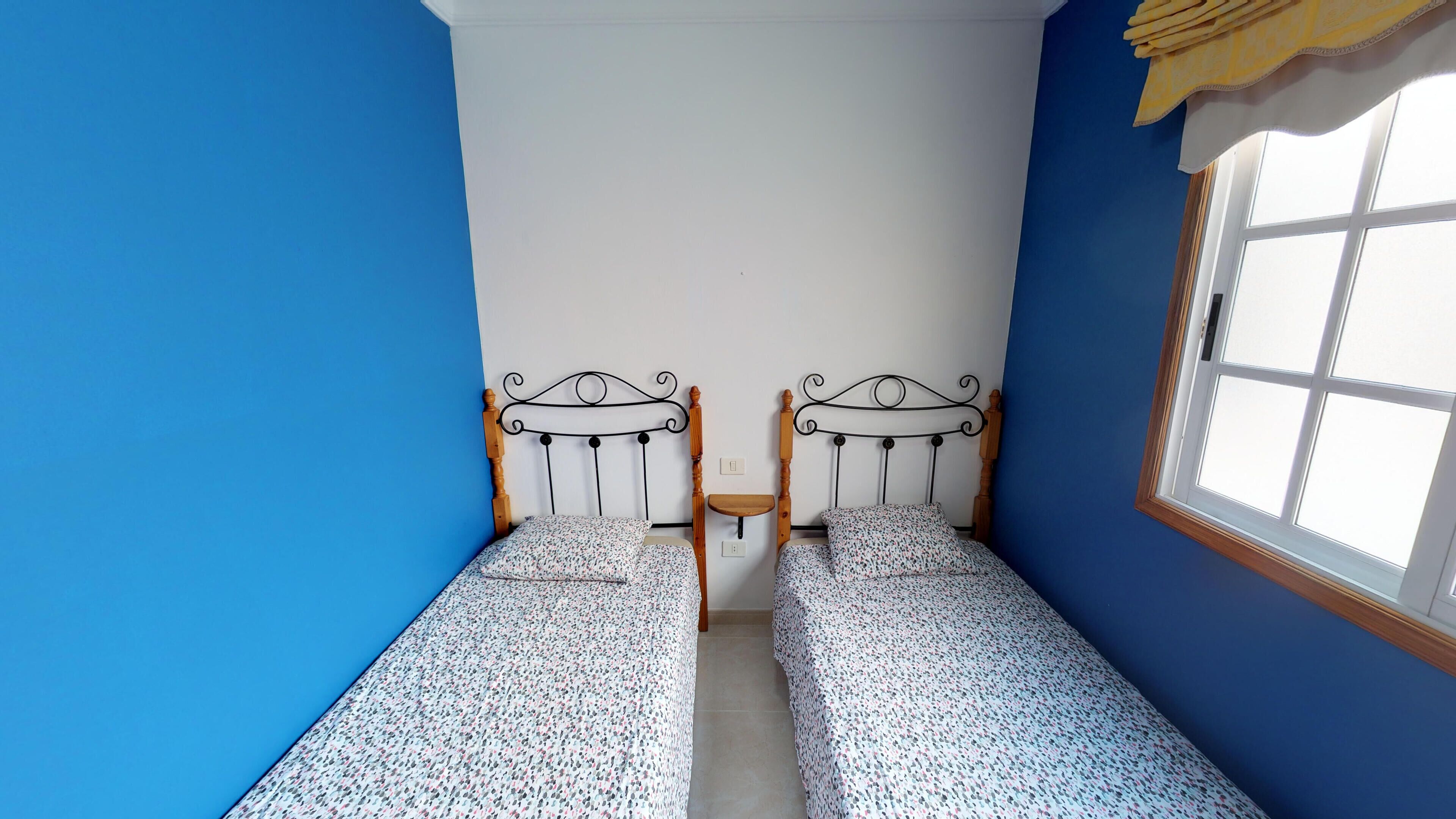 A room with two single beds, a small table, and a window with a view.