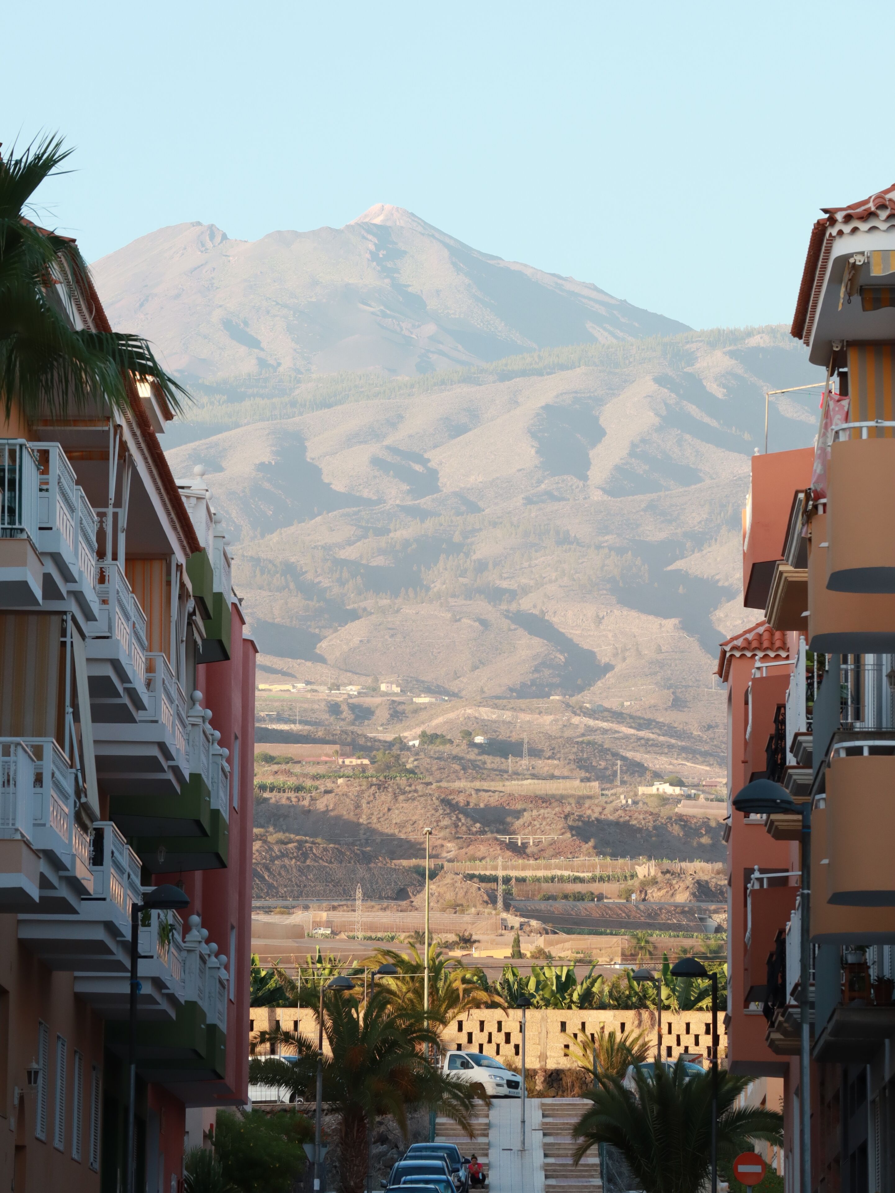Vista de carrer amb una muntanya al fons, amb edificis d'alguns pisos i balcons.
