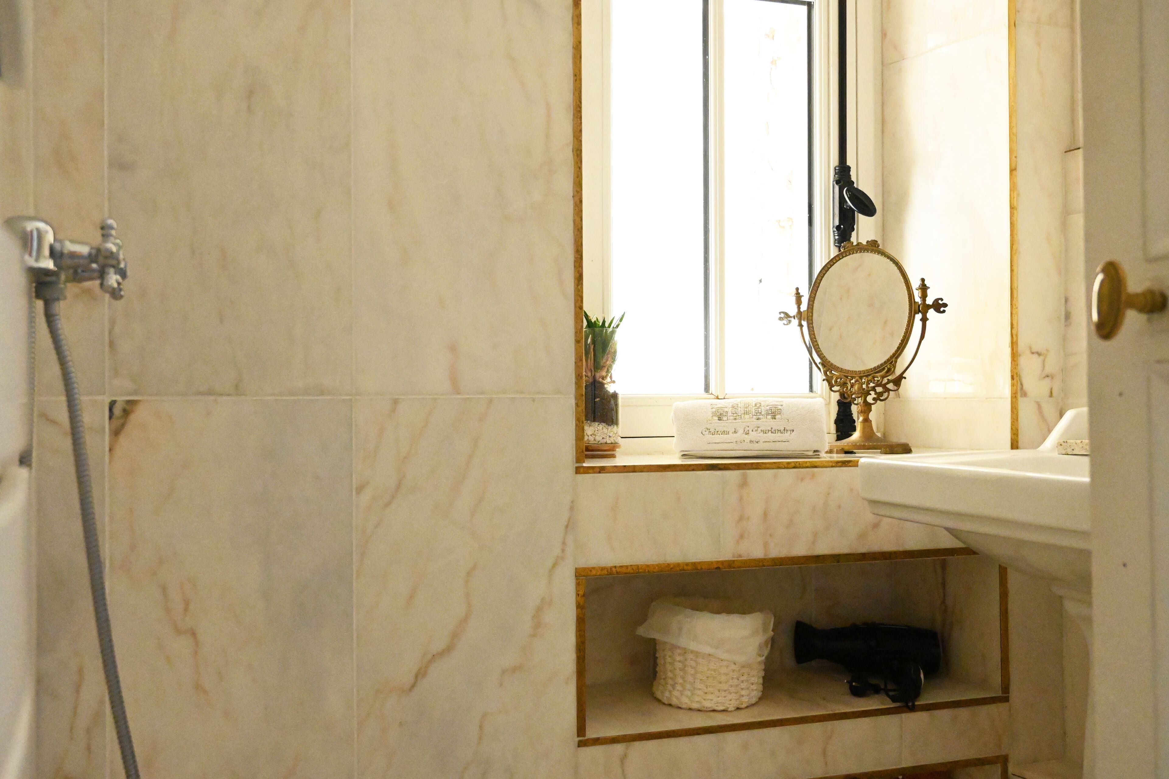 A bathroom with a marble wall, a sink, a mirror, and a towel rack.