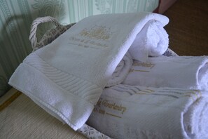 A stack of white towels with gold embroidery, placed on a patterned surface. - Le Chateau De La Tourlandry  (Chemillé-en-Anjou)