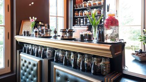 Una zona de bar con diversos vasos y botellas, un tarro grande con una flor rosa, y una estantería con tarros y botellas.
