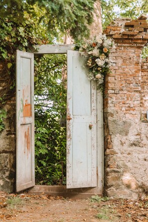 An open rustic wooden door with a brick wall and greenery behind it. - Le Chateau De La Tourlandry  (Chemillé-en-Anjou)