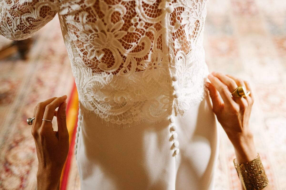 Eine Person trägt ein weißes Spitzenkleid mit tiefem Ausschnitt und steht auf einem gemusterten Teppich.