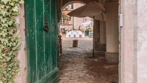 Un corredor de piedra en arco con una puerta verde, que conduce a un patio con asientos al aire libre.