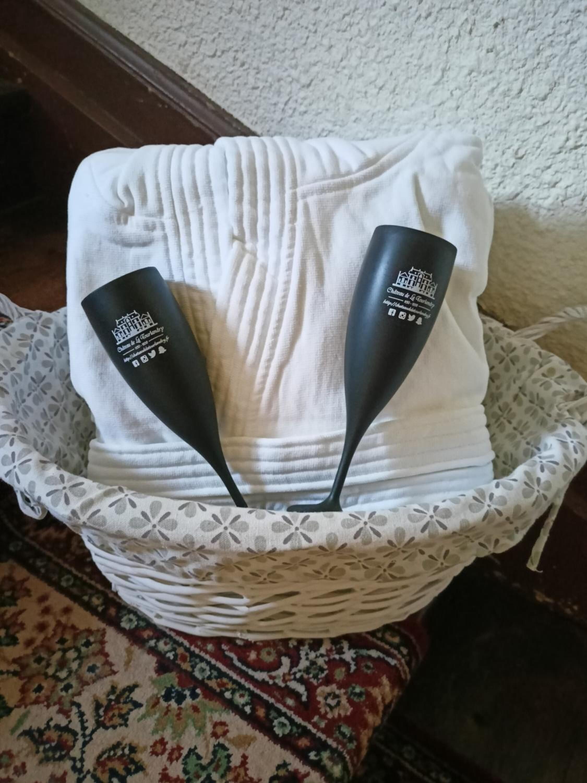 A white towel folded neatly in a basket with two black handles, placed on a patterned rug.
