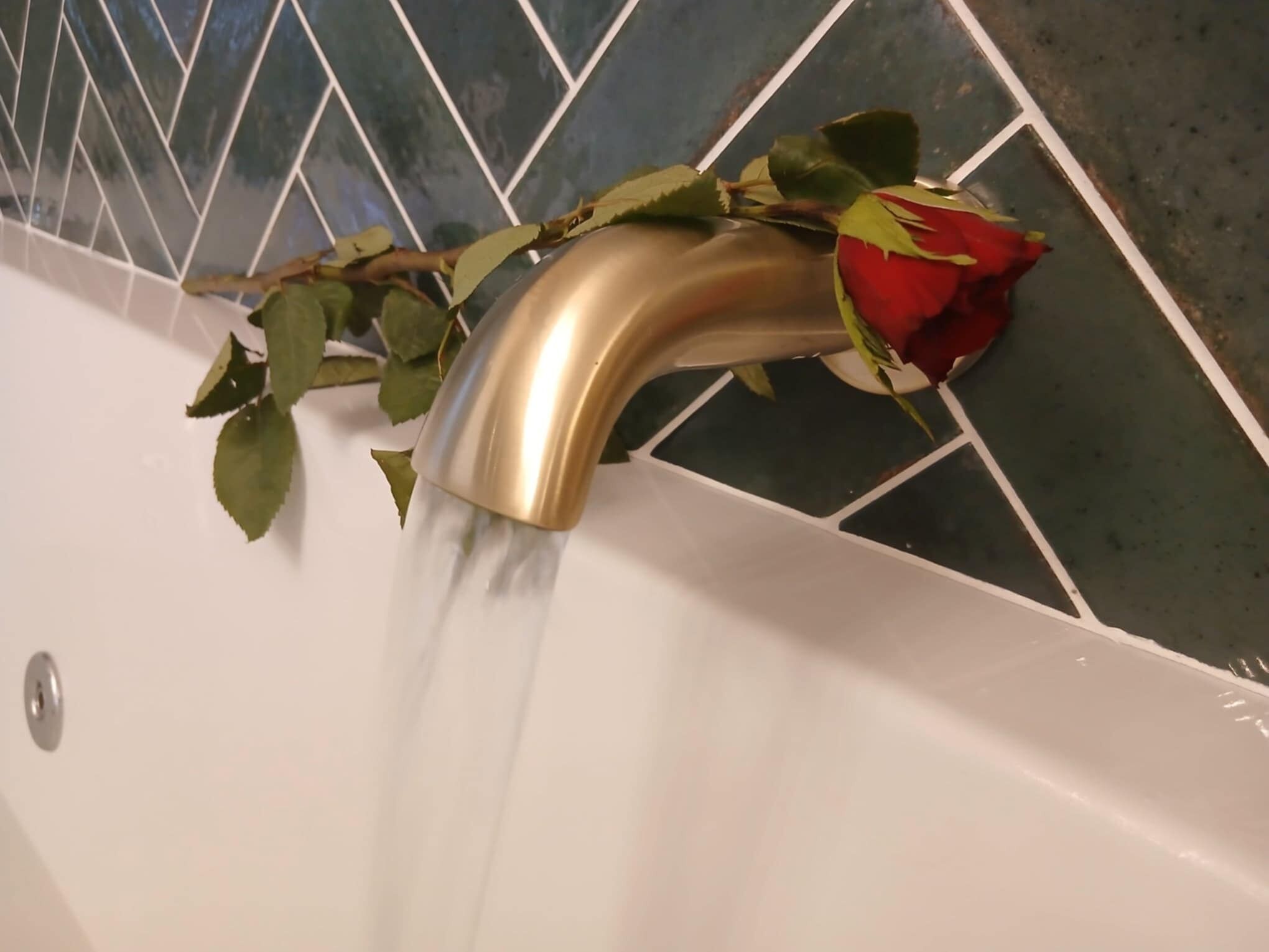 A bathtub with a gold faucet and a red rose resting on it.