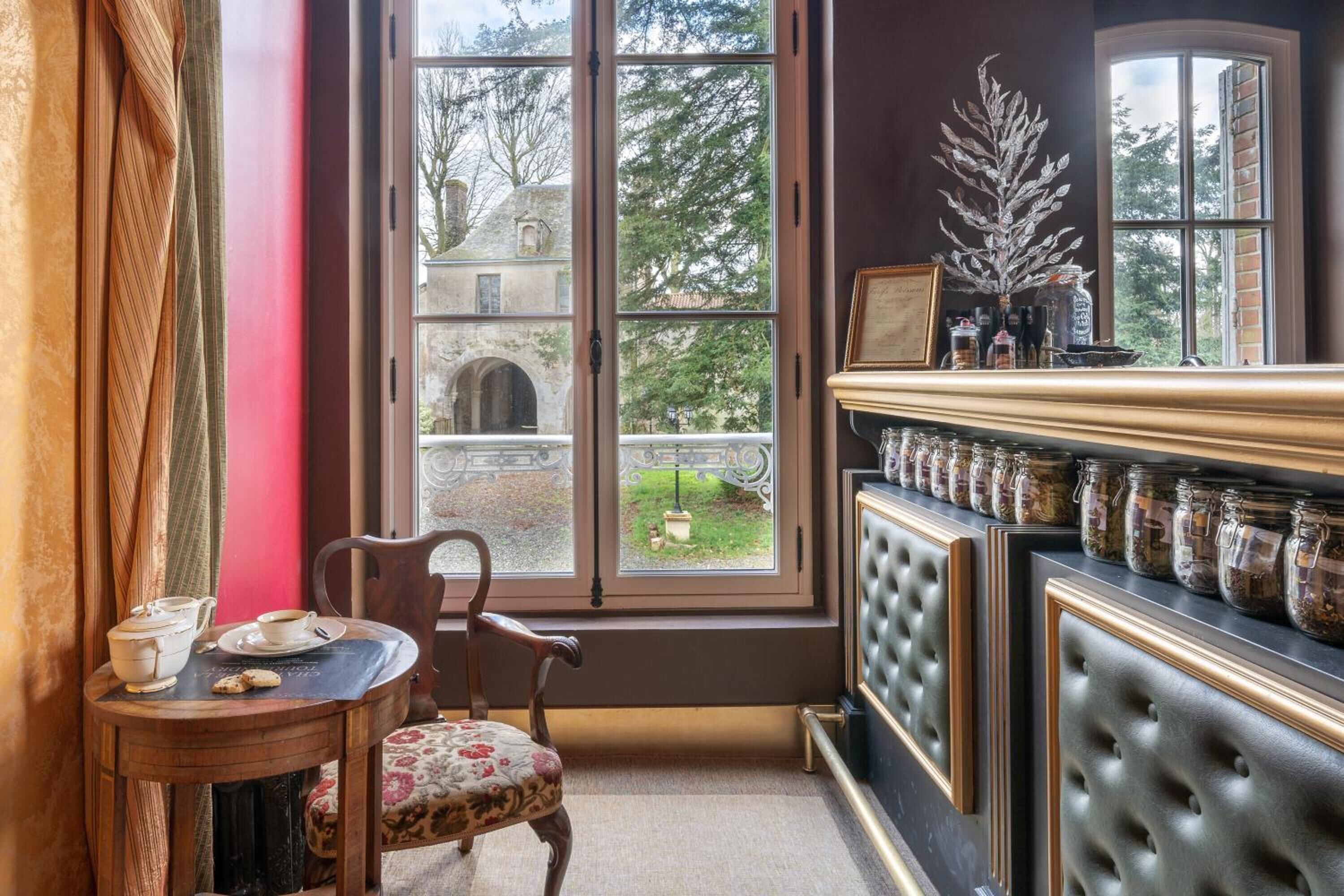 A cozy room with a large window, a wooden chair, a small table with tea set, and a shelf with jars.