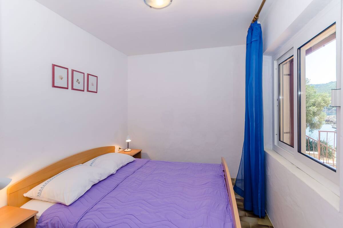 A bedroom with a bed, a nightstand, a window with a view, and three framed pictures on the wall.