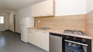A modern kitchen with light-colored cabinets, a built-in dishwasher, a gas stove, and a sink. - Apartments Nedeljko (Gdinj)