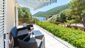 A balcony with wicker furniture, a striped awning, and a view of a lake and hills. - Apartments Nedeljko (Gdinj)